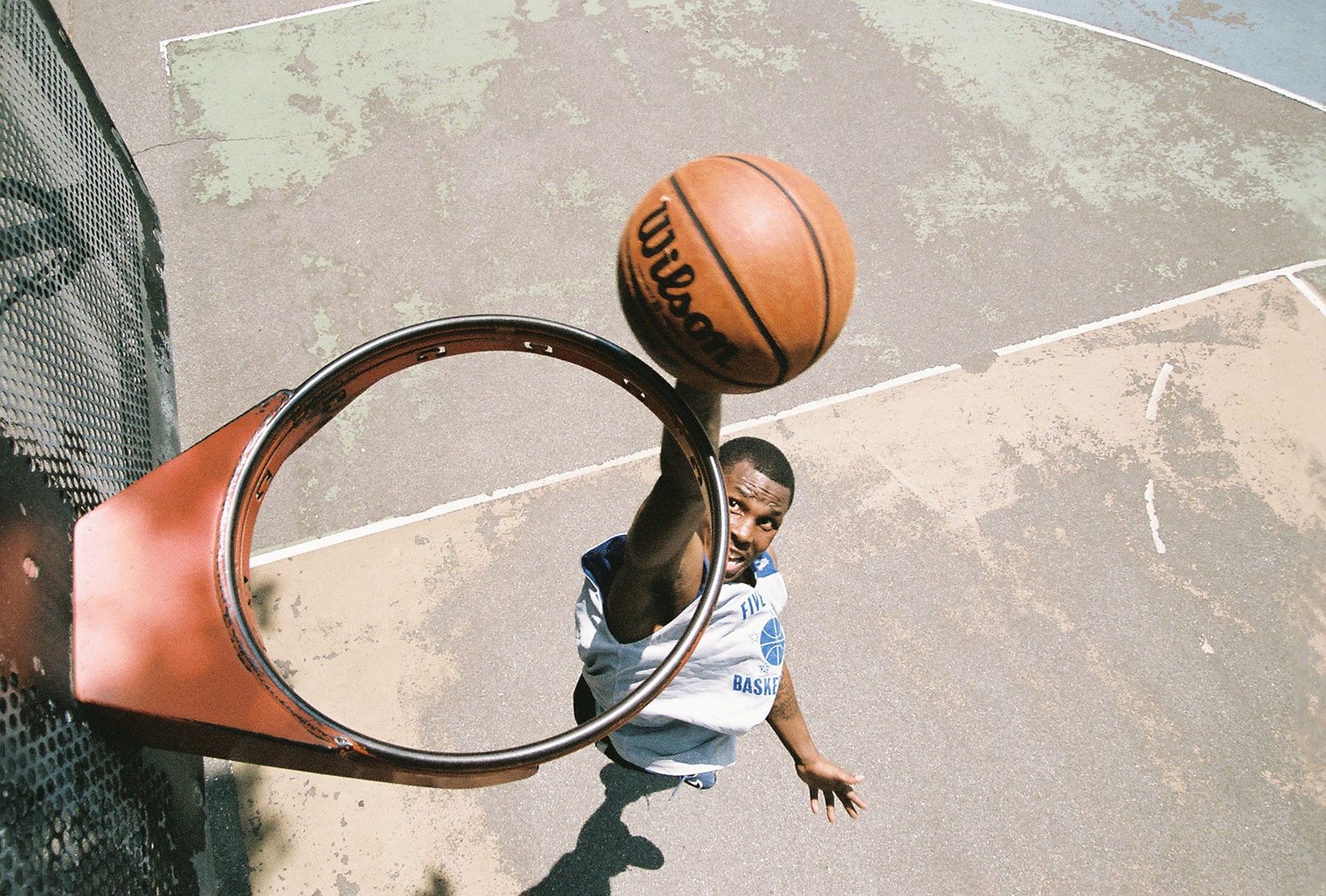 View from above a basketball hoop without a net, where a player is seen about to dunk a basketball through the hoop